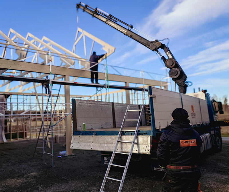 Kranbil som lyfter en takstol på plats vid ett husbygge